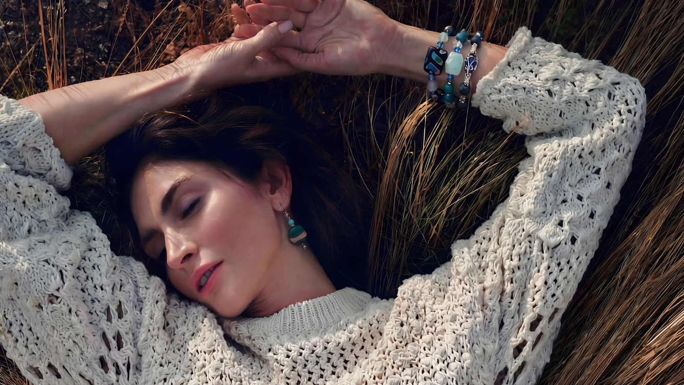 Woman lying on grass wearing a textured sweater, bracelets, and earrings.
