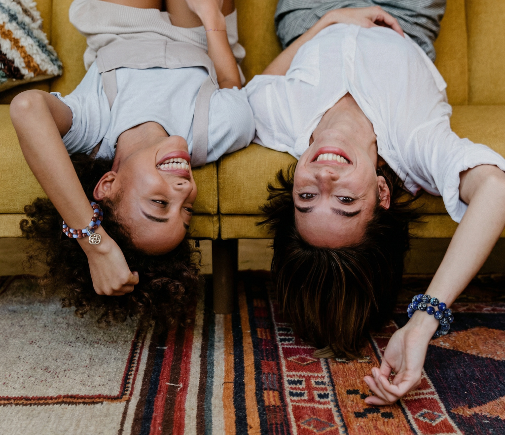 Two people lying on a yellow couch with their heads hanging off, smiling.